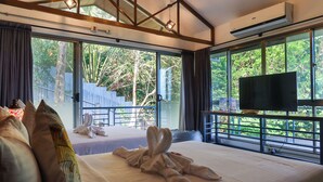 A hotel room with a large bed, a flat-screen TV, and a balcony with a view of greenery. - AV Suites (Puerto Galera)