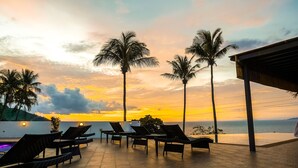 A terrace with lounge chairs and a view of the sunset over the sea. - AV Suites (Puerto Galera)