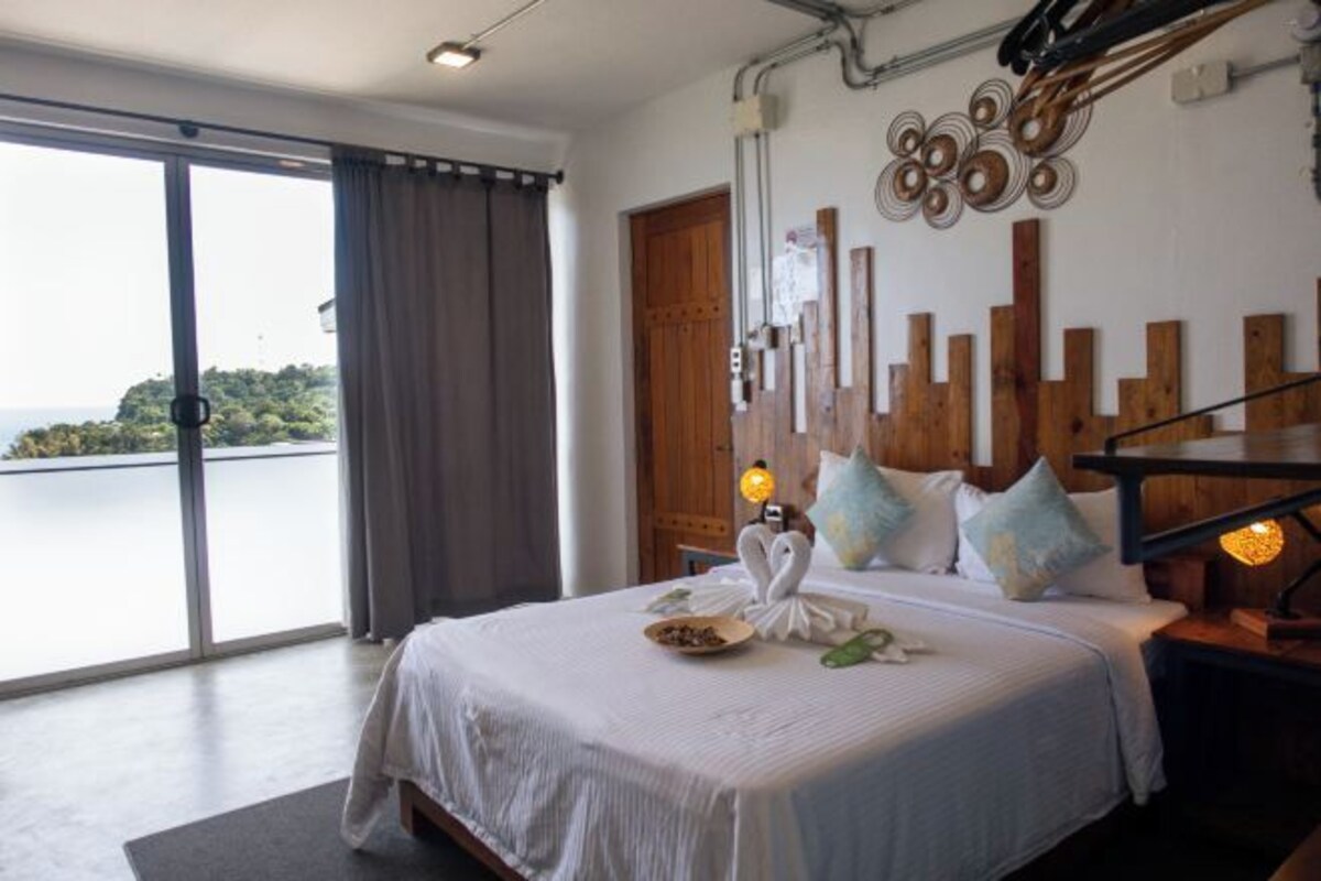 A bedroom with a bed, a view of the sea, and a wooden wall decoration.