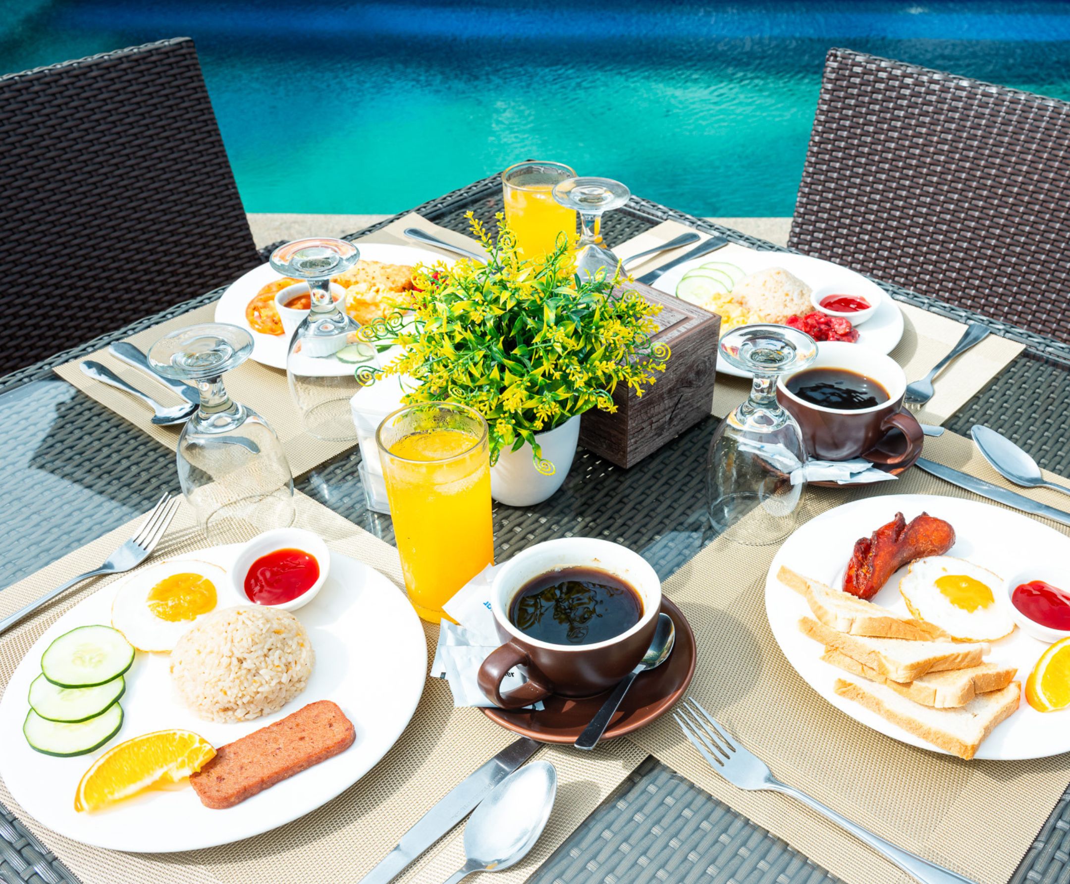 Desayuno con una mesa junto a una piscina, que incluye platos de comida, bebidas y un centro de mesa con flores.