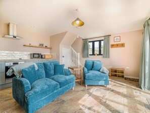 A cozy living room with a blue sofa, a small wooden table, and a kitchen area with a microwave and oven. - The Old Stable At Henley View (Draycott, near Cheddar)