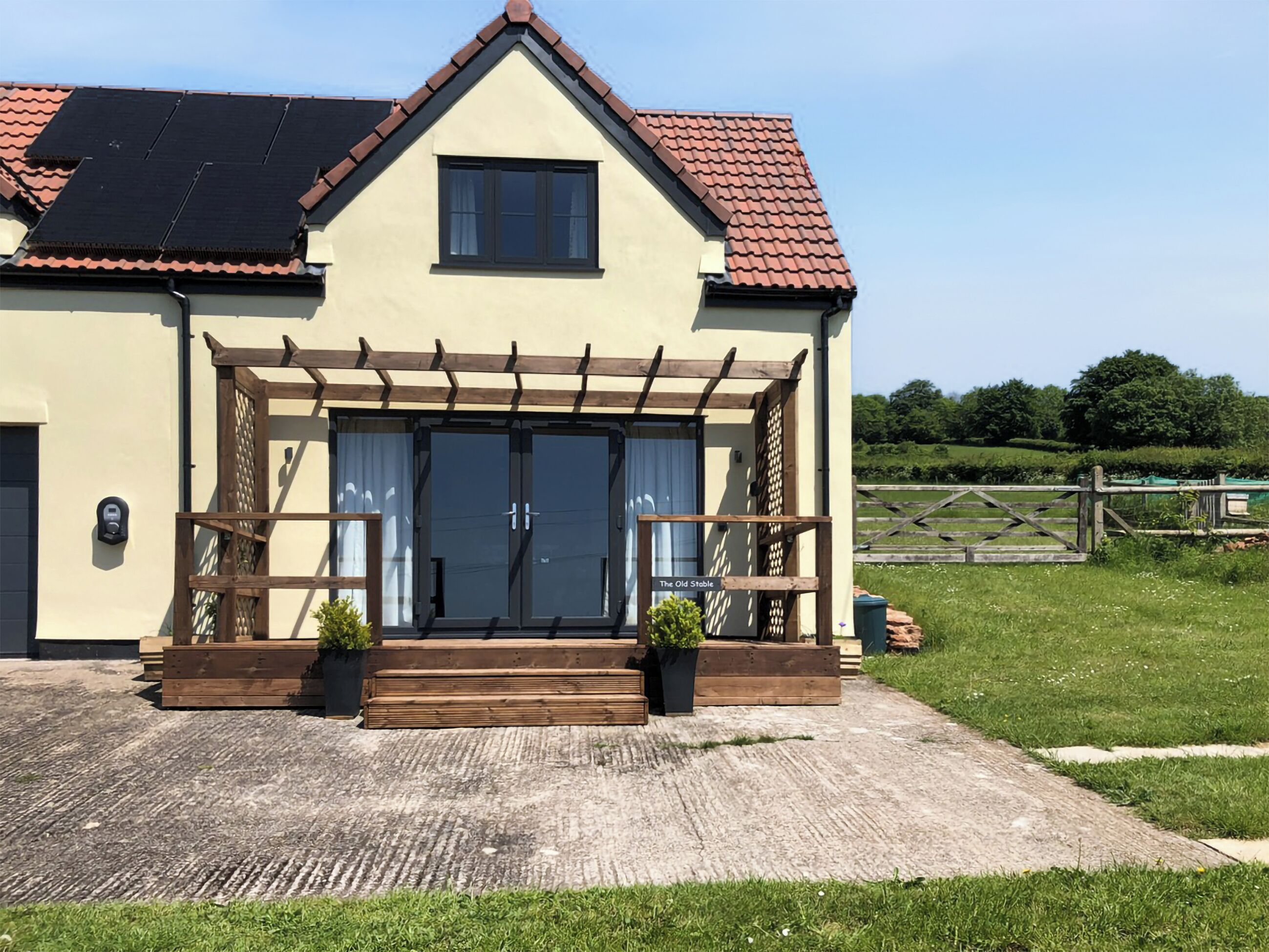 A two-story building with a pitched roof, a covered entrance with a wooden pergola, and a small garden area with potted plants.