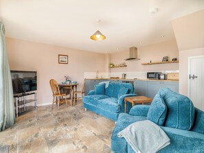 A living room with a blue sofa, a television, and a dining area with chairs and a table.