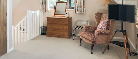 A bedroom with a wooden dresser, a chair, a mirror, a television on a tripod, and a window with curtains.