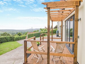 A wooden deck with outdoor seating, a view of the countryside, and a building with large windows. - The Old Stable At Henley View (Draycott, near Cheddar)