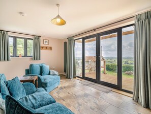 A modern living room with a blue sofa, a pendant light, and a view of the outdoors through large sliding glass doors.