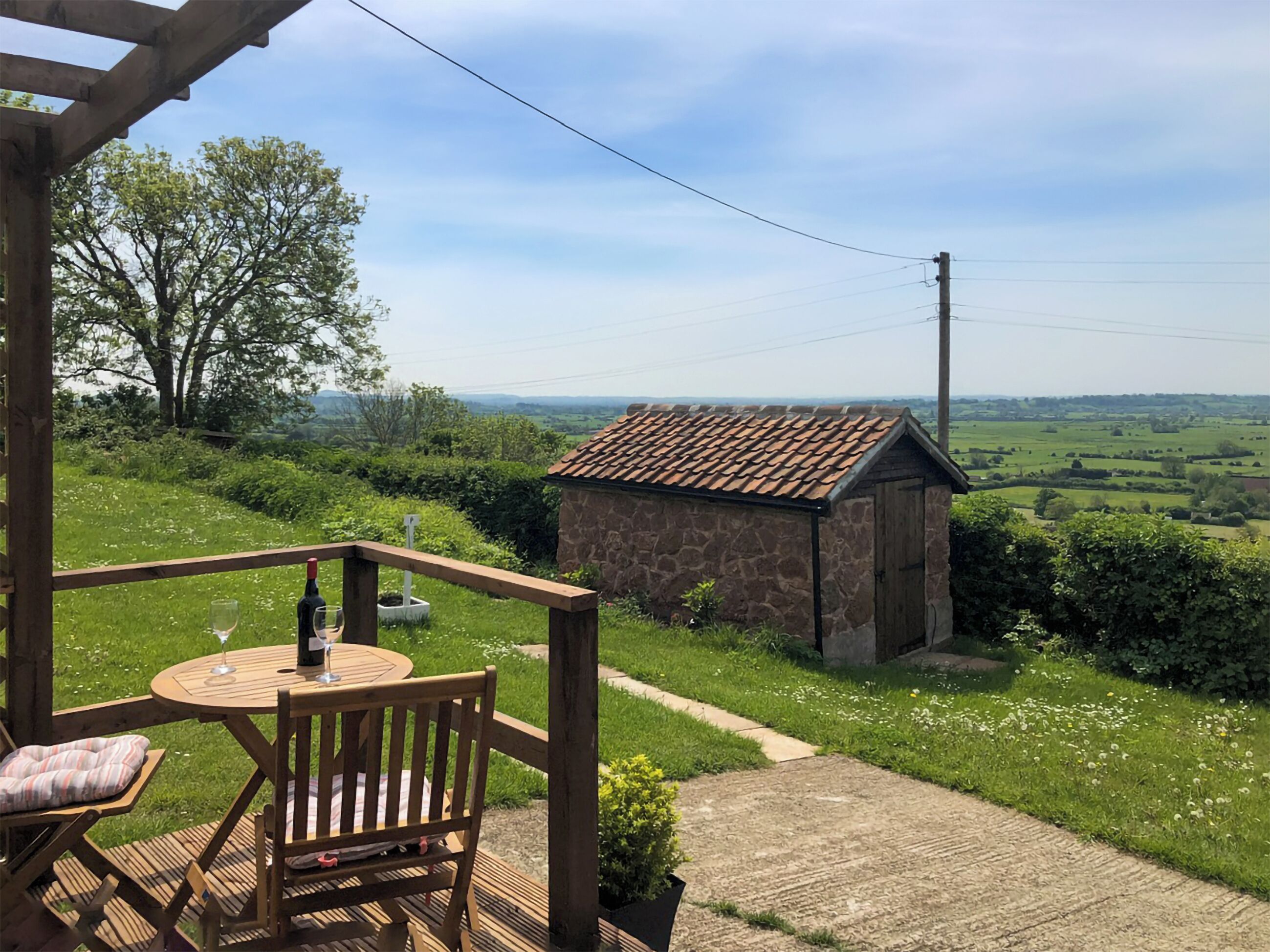 Une terrasse en bois avec une table et des chaises, un bâtiment en pierre et une vue sur la campagne.