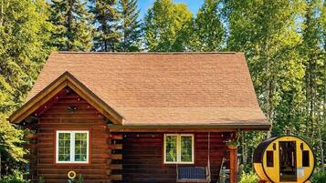 A log cabin with a pitched roof, a front porch, and a circular structure to the right.