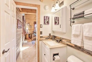 A bathroom with a sink, mirror, towel rack, and artwork on the wall.