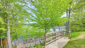 A wooden deck leading to a lake with a view of the water and trees.