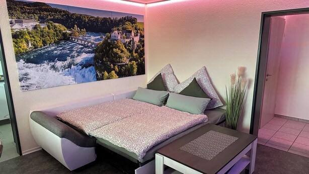 Quarto moderno com cama, mesa de cabeceira e uma grande pintura de paisagem na parede.
