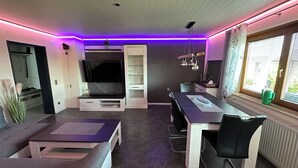 Uma sala de estar moderna com televisão de tela plana, uma mesa de jantar com cadeiras e um espaço de estar aconchegante.
