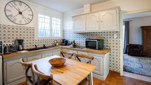 A kitchen with white cabinets, a wooden dining table, and a large wall clock.