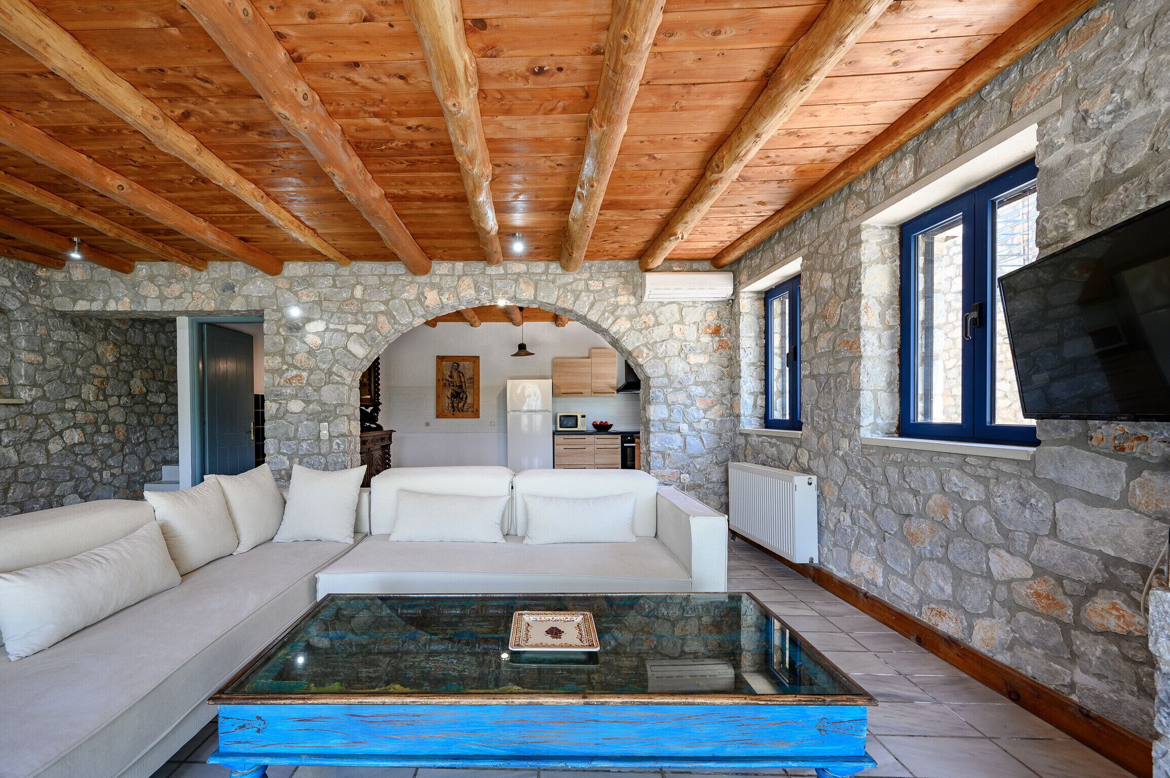 A cozy living area with a stone wall, wooden ceiling beams, a white sofa, and a glass coffee table.