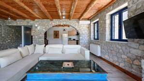 Un salon chaleureux avec un mur en pierre, des poutres apparentes en bois au plafond, un canapé blanc et une table basse en verre.