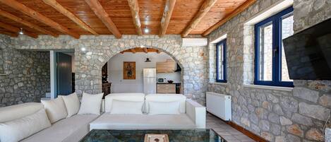 A cozy living area with a stone wall, wooden ceiling beams, a white sofa, and a glass coffee table.