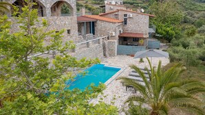 Une villa en pierre dotée d’une piscine, entourée d’une végétation luxuriante et de montagnes.