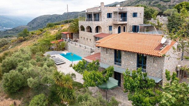 Une maison en pierre avec une piscine, entourée de verdure et de collines.