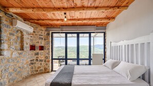 A bedroom with a stone wall, a wooden ceiling, a large bed, and a view of the countryside. - Petritis,serene villa,pool,Near taverns,Crete,Greece (Lampini)