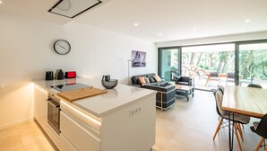 Une cuisine moderne dotée d’un îlot central, d’un coin repas avec une table et des chaises en bois, et d’un espace détente avec un canapé et des fauteuils.