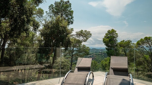 Deux fauteuils inclinables à structure métallique et assise en tissu, placés sur un sol carrelé, avec une balustrade en verre donnant sur un paysage pittoresque.