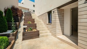 Un bâtiment moderne avec un escalier en béton menant à une porte. Des jardinières en bois, ornées de plantes, sont disposées le long des marches.