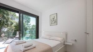 Une chambre moderne avec un grand lit, une table de chevet, une fenêtre donnant sur des arbres et un tableau encadré au mur.