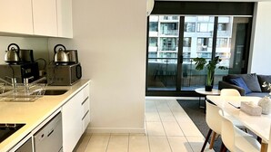 A modern kitchen with stainless steel appliances, a dining area with a white table and chairs, and a large window offering a view of a cityscape. - Incredible 2 BR City Apartment (Melbourne)