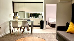 A modern living room with a round wooden coffee table, a grey sofa with a yellow pillow, and a dining area with a glass table and chairs.