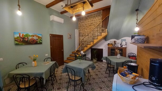 A dining area with tables and chairs, a staircase, and a painting on the wall.