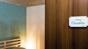A bedroom with a bed, pillows, and a wooden door with a sign reading "camera Casalotto".