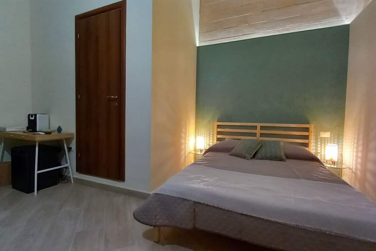 A bedroom with a bed, bedside lamps, a desk, and a wardrobe.