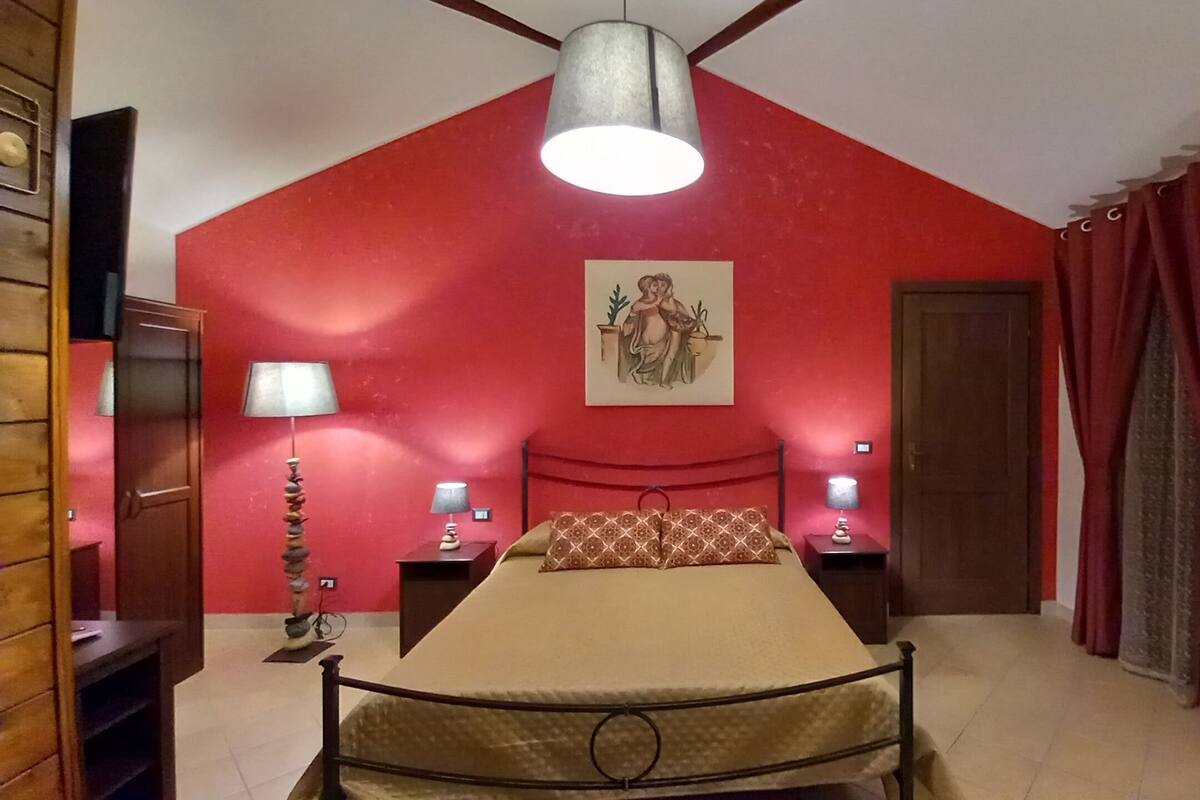 A bedroom with a red ceiling, a bed with a headboard, two bedside tables with lamps, and a door.