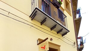 A building with a brown door, a small balcony with a metal railing, and a sign above the door.