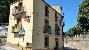 A multi-story building with balconies, a sign indicating a sports field direction, and a small entrance door.