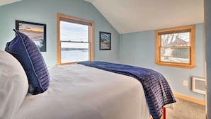 A bedroom with a large bed, two windows, and artwork on the walls.
