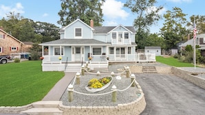 A two-story house with a front porch, a small garden with a flower bed, and a flagpole.