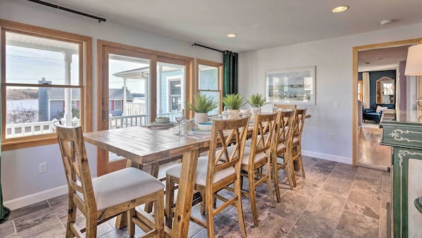 A dining area with a wooden table and chairs, large windows, and a view of the outside.