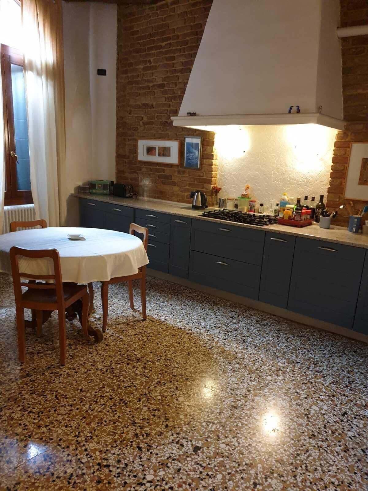 A kitchen with a granite countertop, a gas stove, and a white hood above the stove. There is a dining table with chairs in the foreground.