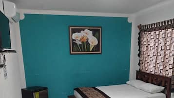Quarto de hotel com duas camas de madeira, uma pequena lixeira, uma luminária no teto e um quadro pendurado na parede.