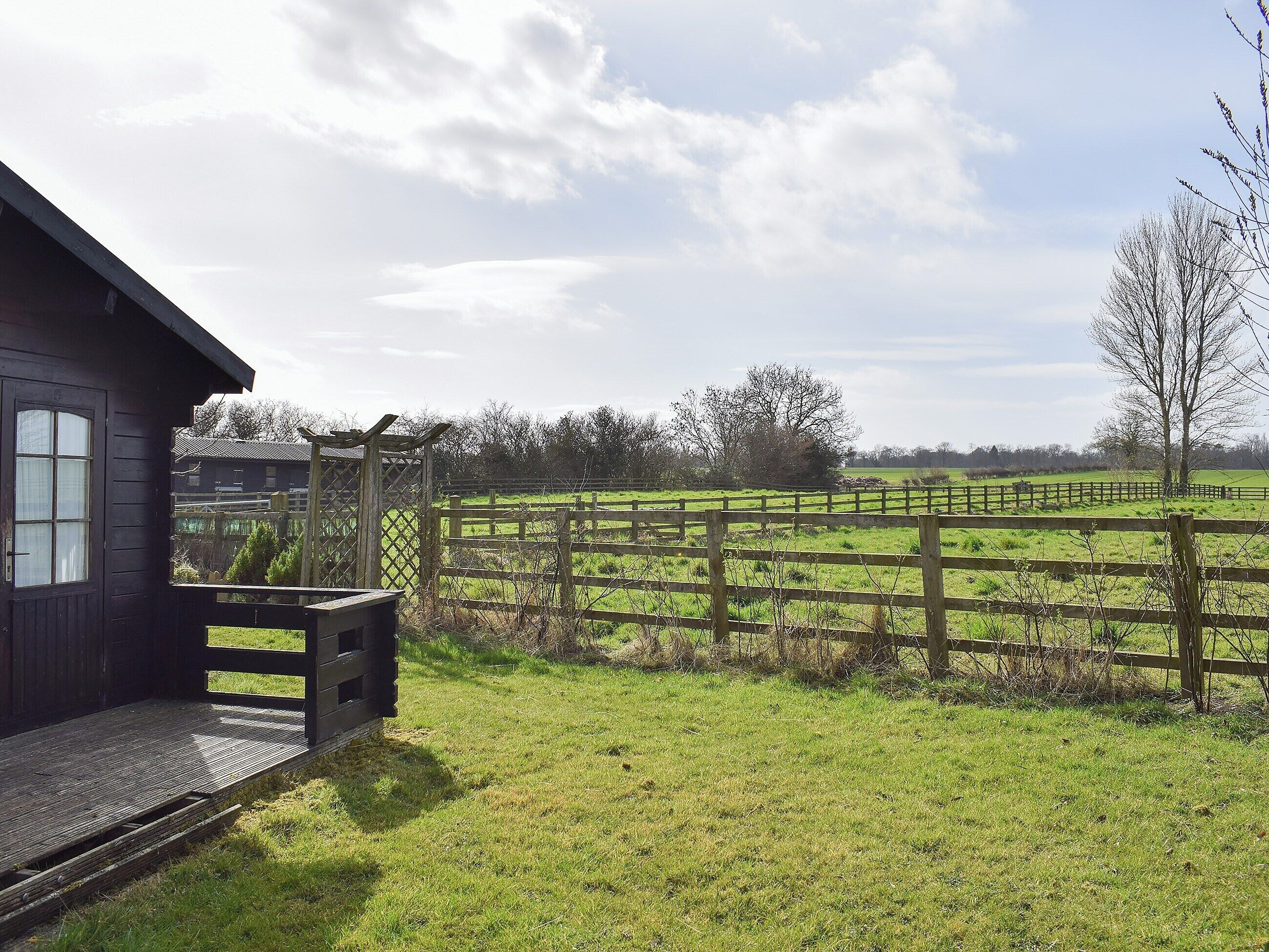 A rustic wooden house with a porch and a view of a fenced pasture.