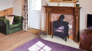 A cozy living room with a green leather sofa, a fireplace with a brick facade, and a large mirror above it. - 2 bedroom accommodation in Thirkleby, near Thirsk (Thirkleby, near Thirsk)