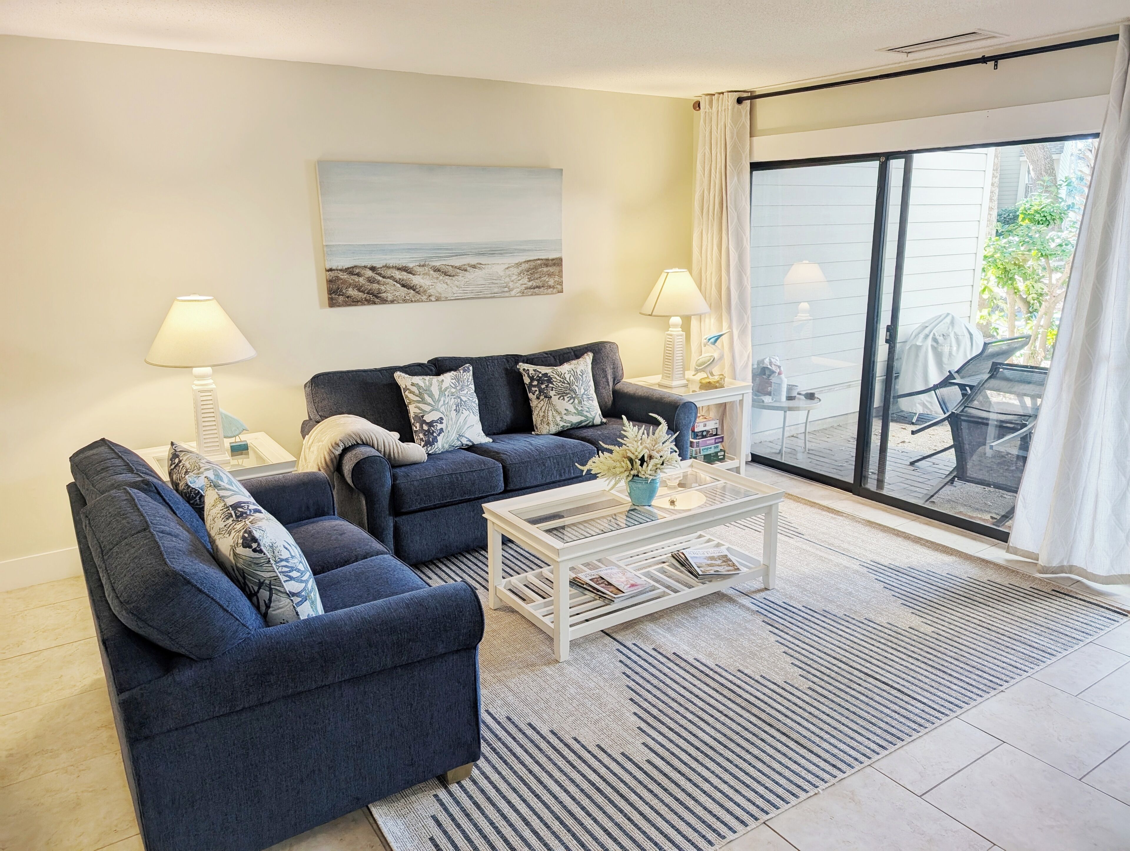Een woonkamer met twee donkerblauwe banken, een witte salontafel en een schilderij van een strandgezicht.