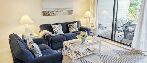 Een woonkamer met twee donkerblauwe banken, een witte salontafel en een schilderij van een strandgezicht.