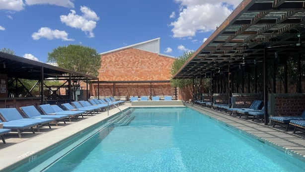 Una piscina con sillas de descanso y un edificio de ladrillo al fondo.