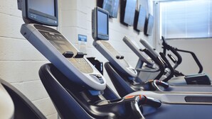 Varias bicicletas estáticas alineadas en un gimnasio, con pantallas digitales encima de cada una.