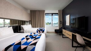 Habitación de hotel con dos camas, un escritorio, una silla, un televisor y una ventana con cortinas.