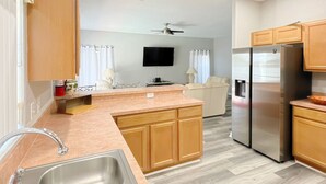 A modern kitchen with a central island, stainless steel appliances, wooden cabinets, and a flat-screen TV mounted on the wall. - High Grove Hideaway, Spacious 5BR Villa w/ Pool Near Disney (Four Corners)