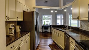 A kitchen with white cabinets, a refrigerator, a coffee maker, and a window.