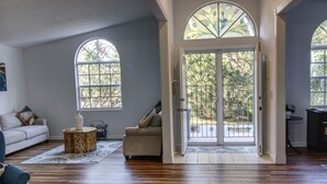 A spacious living room with hardwood flooring, a sofa, a coffee table, and a large arched doorway leading outside.